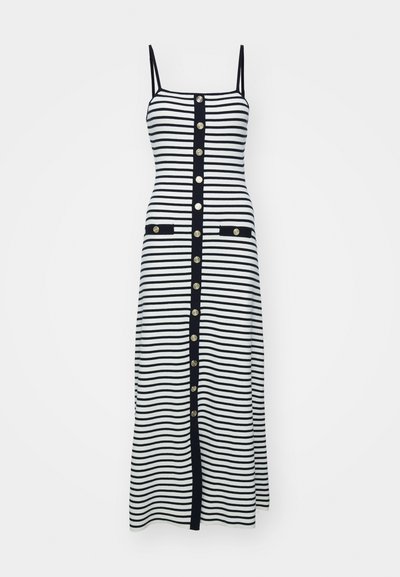 Gestreiftes Midi-Kleid in Schwarz und Weiß mit schmalen Trägern, goldenen Knöpfen entlang der Vorderseite und zwei vorne liegenden Taschen, die in Schwarz eingefasst sind.