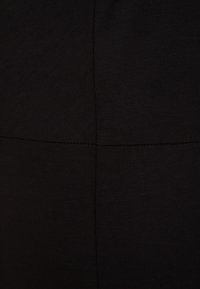 Svart, figurnära tyg med en jämn textur och subtil sömdetaljering. Har en minimalistisk design utan mönster eller detaljer.