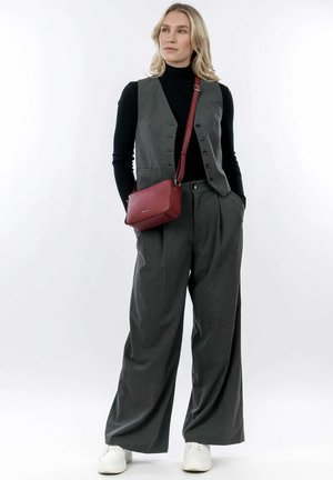Gilet grigio su misura sopra un dolcevita nero, abbinato a pantaloni grigi a gamba larga e sneakers bianche. È inclusa una piccola borsa a tracolla rossa con texture.