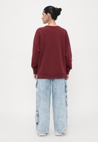 Sweatshirt oversized em bordô com decote redondo, combinado com calças largas de cargo azul claro, com bolsos laterais e cordões.