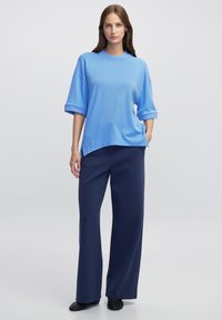 Světle modré oversized tričko s krátkým rukávem a kulatým výstřihem, spárované s tmavě námořnickými kalhotami s širokými nohavicemi, které mají hladkou texturu.
