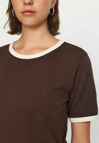 Brun kortærmet t-shirt med en kontrastfyldt cremefarvet ribbet krave og ærmekanter, lavet af blødt bomuldsstof med en glat tekstur.