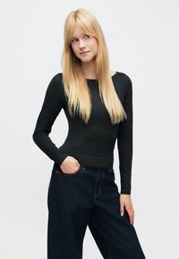 Fekete, hosszú ujjú felső kerek nyakkivágással, sima anyagból, sötét széles szárú farmernadrággal, oldalzsebekkel párosítva.