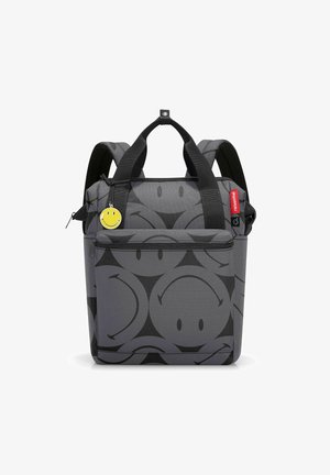 Grauer Rucksack mit einem Smiley-Gesicht-Design, zwei oberen Griffen, gepolsterten Schulterriemen und einem gelben Smiley-Anhänger. Hat eine vordere Reißverschlusstasche.