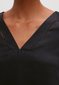 Maglietta nera con scollatura a V, caratterizzata da tagli sottili lungo il collo, realizzata in un tessuto liscio e strutturato.