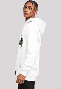 Balta kapuce ar lielu, krāsainu sikspārņa formas logotipu uz krūtīm. Materiāls izskatās mīksts, ar priekšējo kabatu un saites kapuci.