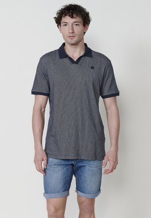 Polo bleu marine à motifs avec un col en V et un col contrastant, associé à un short en denim bleu clair aux manches retroussées.