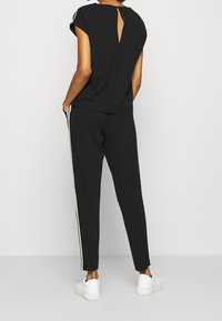 Czarna koszulka z tylnym wycięciem w kształcie klucza, zestawiona z czarnymi spodniami z białymi paskami po bokach i białymi sneakersami. Miękka tkanina i luźny krój.