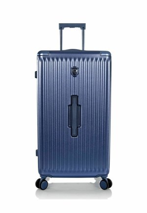 Grande valise rigide bleu marine avec des rainures verticales, quatre roues multidirectionnelles, poignée rétractable et poignée avant.