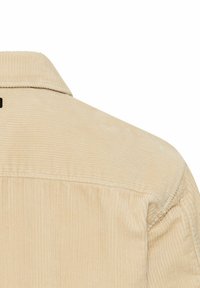 Beige corduroy overhemd met een kraag, met verticale ribbels en een gladde textuur. Opvallende stikdetails op de achterkant.