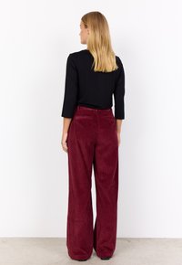 Black long-sleeve top and burgundy corduroy wide-leg pants with vertical ribbed texture, elastic waistband, and back pockets.