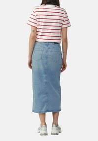 Gestreepte rood en witte cropped t-shirt gecombineerd met een lichtblauwe denim midi rok met een rechte snit en achterzakken. Gekleed met grijze sneakers.