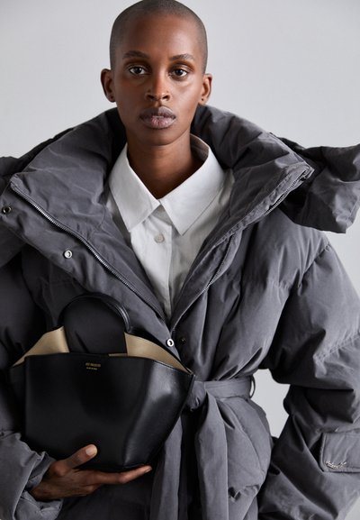 Gray puffer jacket with a high collar and tied waist, paired with a black leather handbag featuring a rounded handle and beige interior.