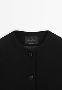Manteau noir avec encolure ronde et deux boutons noirs, avec une étiquette Massimo Dutti indiquant « fabriqué au Portugal ».