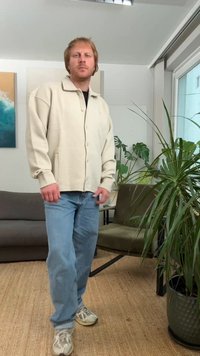 Giacca beige chiaro con bottoni e motivo testurizzato, abbinata a jeans azzurri e sneaker grigie in un ambiente interno casual.