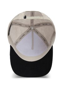Gorra de béisbol con una parte superior de tela beige, visera negra y forro interior con un patrón de texto repetido. Correa ajustable visible en el interior.