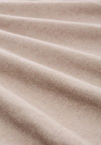 Tissu beige clair avec une texture lisse et douce, présentant de subtils plis et un tissage fin et uniforme sur toute la surface.