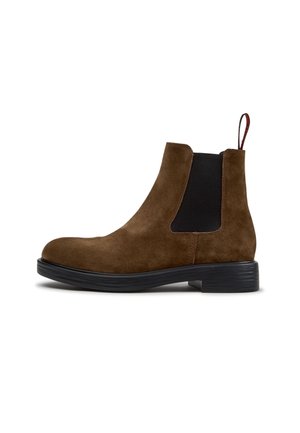 Brun ruskind Chelsea-støvle med sort elastisk sidepanel, sort sål, lav hæl og trækflig bagpå.