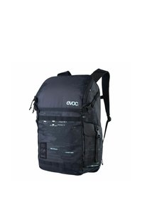 Mochila negra con una superficie texturizada, que presenta un patrón geométrico en tonos negro y verde azulado, correas ajustables y dos bolsillos con cremallera.