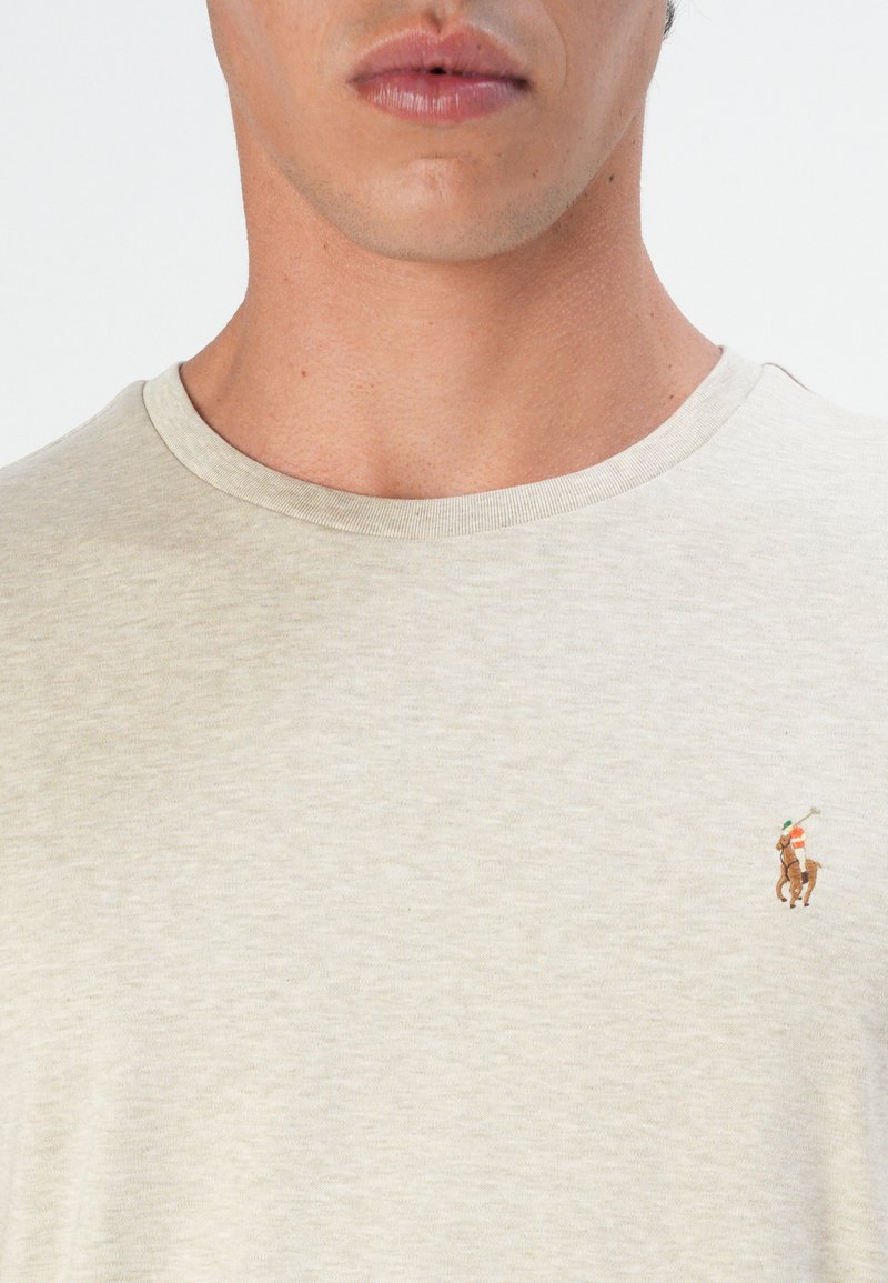 Camiseta de algodón ligera en color beige claro para hombre con cuello redondo. Presenta un pequeño logo bordado en el lado izquierdo del pecho que representa a un golfista y un caballo.