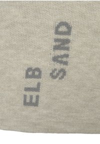 Tessuto a maglia beige con grande testo grigio, parzialmente oscurato, con un aspetto strutturato. Il design è minimale e ripetitivo.