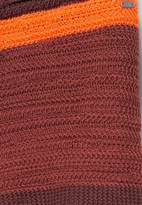 Tissu tricoté avec de larges rayures horizontales en marron, marron foncé et une rayure orange près du haut avec une petite étiquette de marque en métal.