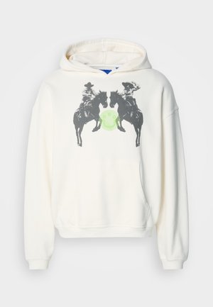 Vit hoodie med en framsidesgrafik av två ryttare på hästar som står mittemot varandra, centrerad över en grön cirkel. Tillverkad av tyg med en mjuk textur.