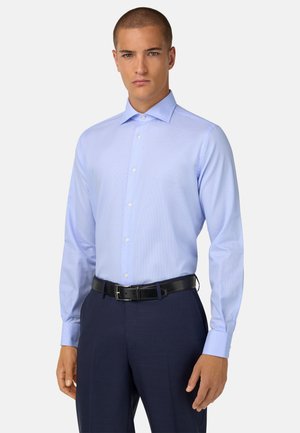 Camicia azzurro chiaro a scacchi, con maniche lunghe e colletto a punta, abbinata a pantaloni scuri a righe e una cintura nera.