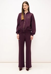 Felpa viola con zip dorato e dettaglio a stella, abbinata a pantaloni larghi coordinati. Entrambi realizzati in un morbido tessuto testurizzato.