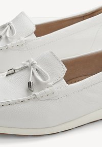 Par de mocasines blancos de cuero con detalle de lazo y punteras metálicas, con acentos cosidos y forro interior acolchado color marrón claro.