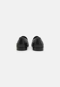 Black leather shoes featuring a woven design, rounded toe, and flat soles. Back view highlights texture and smooth finish.