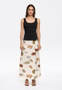 Canotta nera con scollo a quadrato abbinata a una lunga gonna beige con motivi di animali colorati e due tasche a toppa.