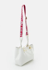 Biała skórzana torebka z złotymi akcentami i odpinanym czerwonym paskiem, na którym znajduje się biały tekst logo Emporio Armani.