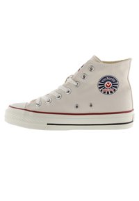 Hoge canvas sneakers in lichtbeige met metalen oogjes, witte rubberen zool, rode streep en een cirkelvormig blauw logo aan de zijkant.