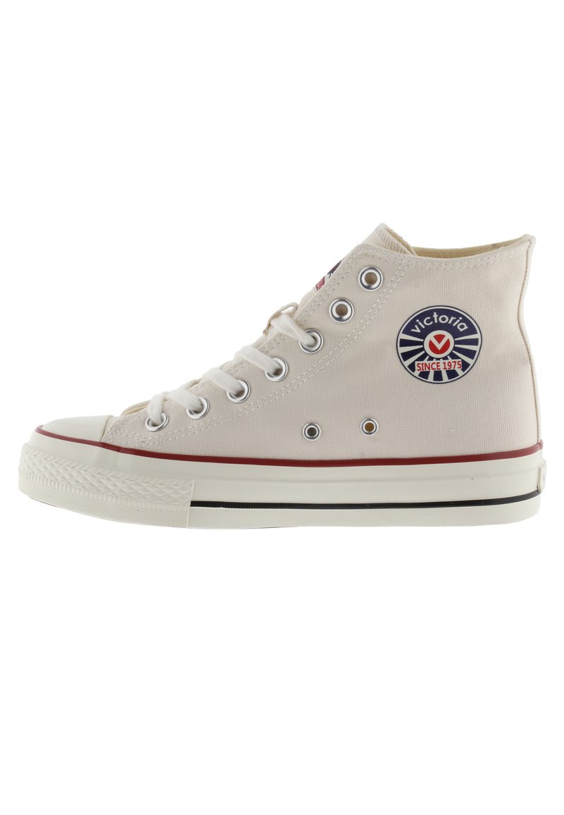 Hoge canvas sneakers in lichtbeige met metalen oogjes, witte rubberen zool, rode streep en een cirkelvormig blauw logo aan de zijkant.