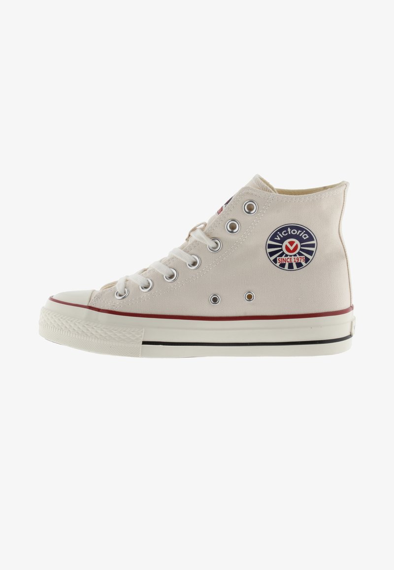 Hoge canvas sneakers in lichtbeige met metalen oogjes, witte rubberen zool, rode streep en een cirkelvormig blauw logo aan de zijkant.