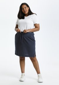 Jupe en lin marine avec taille élastiquée, poches latérales et fente. Associée à un t-shirt blanc à manches courtes et des baskets blanches.
