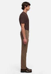 Bruin T-shirt met korte mouwen en ronde hals, gecombineerd met beige slim fit broek en donkerbruine leren schoenen, gezien van opzij.