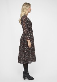 Maxikjole i sort gennemsigtig stof med små røde og lyserøde blomster mønstre, lange ærmer og en smal talje. Sammen med sorte ankelstøvler.