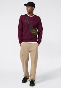 Felpa maroon, pantaloni cargo beige con tasche, scarpe nere, cappellino nero e borsa a tracolla verde. Design semplice con vestibilità casual.