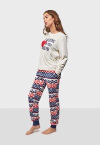 White sweatshirt with "I BELIEVE IN YOU AND ME" text and red heart. Matching joggers with red and blue heart-patterned design. Soft fabric.