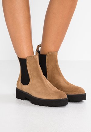 Bottes cheville en daim marron avec panneaux latéraux élastiques noirs et semelles en caoutchouc noir épaisses. Dotées d'une boucle à l'arrière pour un enfilage facile.