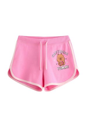 Jonge persoon met bril die een grijs tanktop en roze korte broek draagt met een cartoon capibara met donut en ontspanningstekst, binnenstaand.