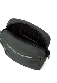 Borsa a spalla verde in nylon con apertura con zip. Presenta un logo bianco sul fronte e una texture liscia. Etichetta interna visibile.