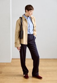 Beige takki, vaaleansininen paita, laivastonsiniset housut ja burgundin väriset lenkkarit. Takissa on laatikkomainen leikkaus ja nappidetaljit; laukku on tyylikäs.