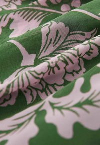 Tessuto verde con un motivo floreale rosa, caratterizzato da grandi foglie e fiori, che presenta una texture liscia e un design fluido.