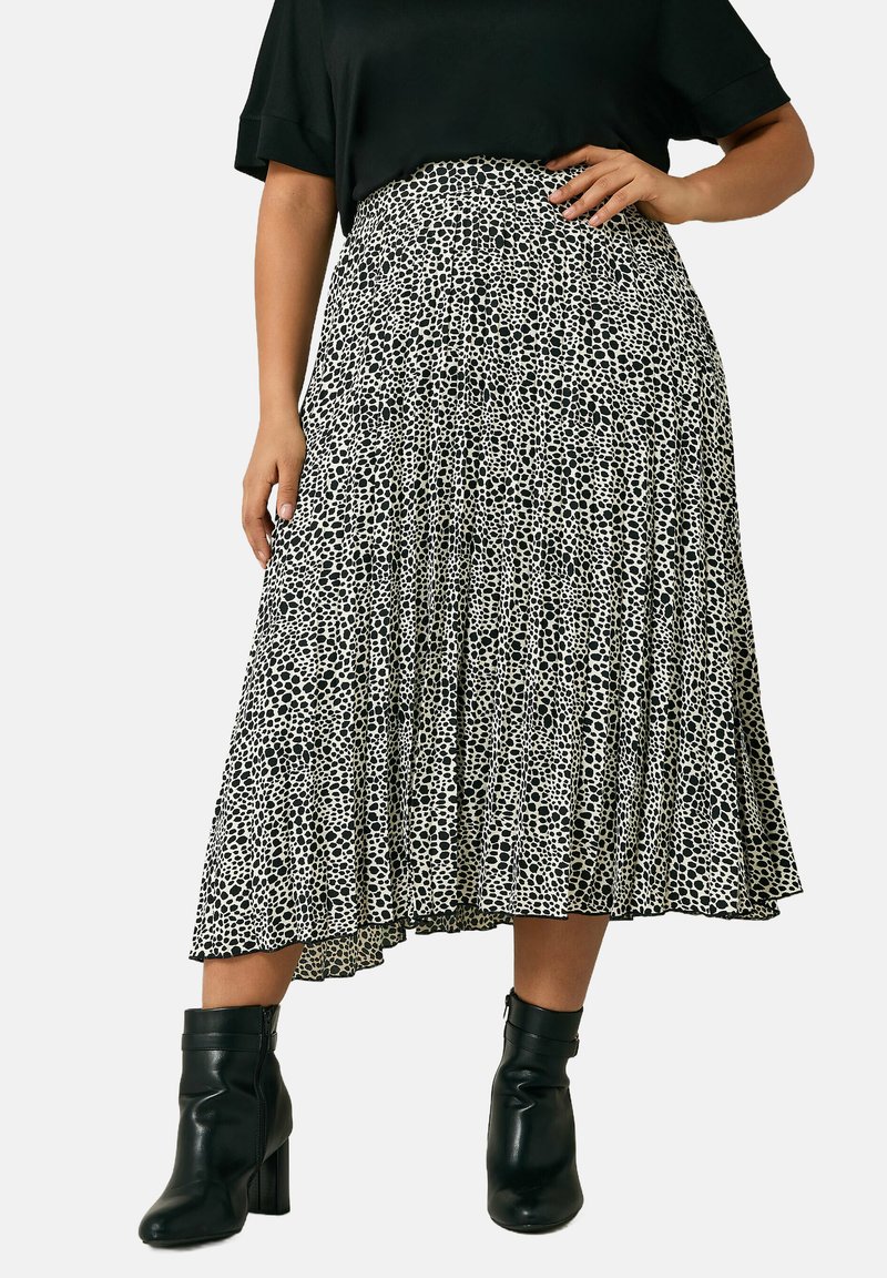 Zwart-witte geplisseerde midi-rok met een stippenpatroon, gemaakt van lichte stof, gecombineerd met zwarte enkellaarsjes.