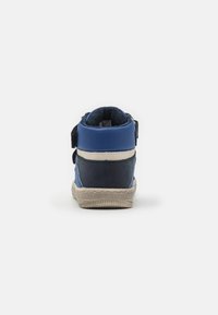 Zapatilla alta azul que combina materiales texturizados y lisos, con una correa de Velcro y una suela de goma de color claro.