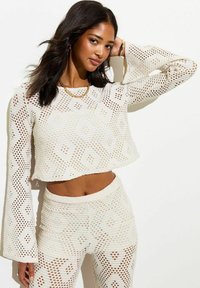 Witte, opengewerkte cropped trui met klokmouwen, voorzien van een diamanten patroon en bijpassende hoge gebreide broek. Textuurstof.