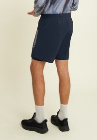 Shorts atletici blu navy con cintura elastica, tasche laterali e dettagli riflettenti. Indossati con sneakers nere e calze grigie.